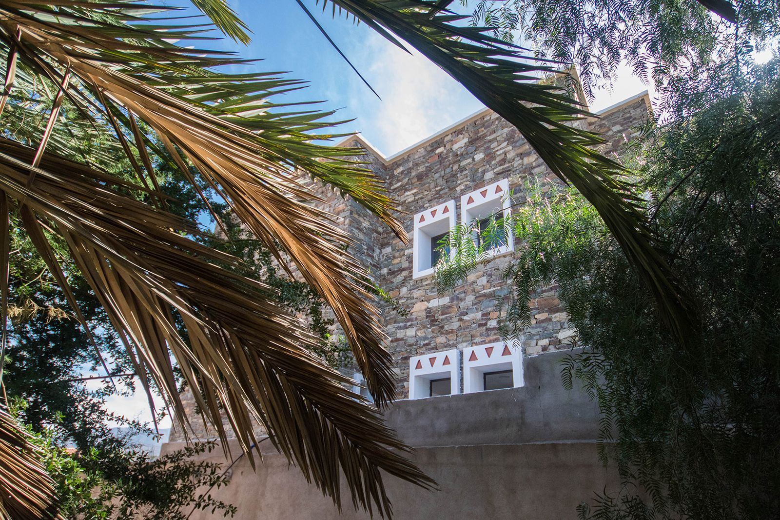 Dar Al Oumouma : façade en pierre aux fenêtres blanches, vue entre les palmes