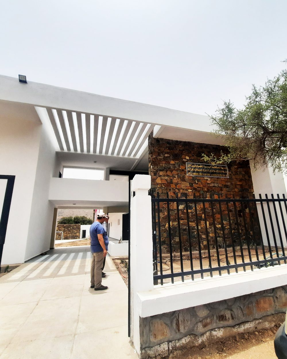 Entrée d'une école : mur en pierre, pergola et volumes blancs