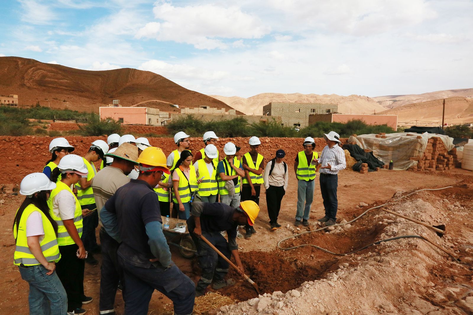 Chantier-école de Taliouine : étudiants de l'ENA Agadir et artisans autour des fondations, adobes en séchage et montagnes en arrière-plan