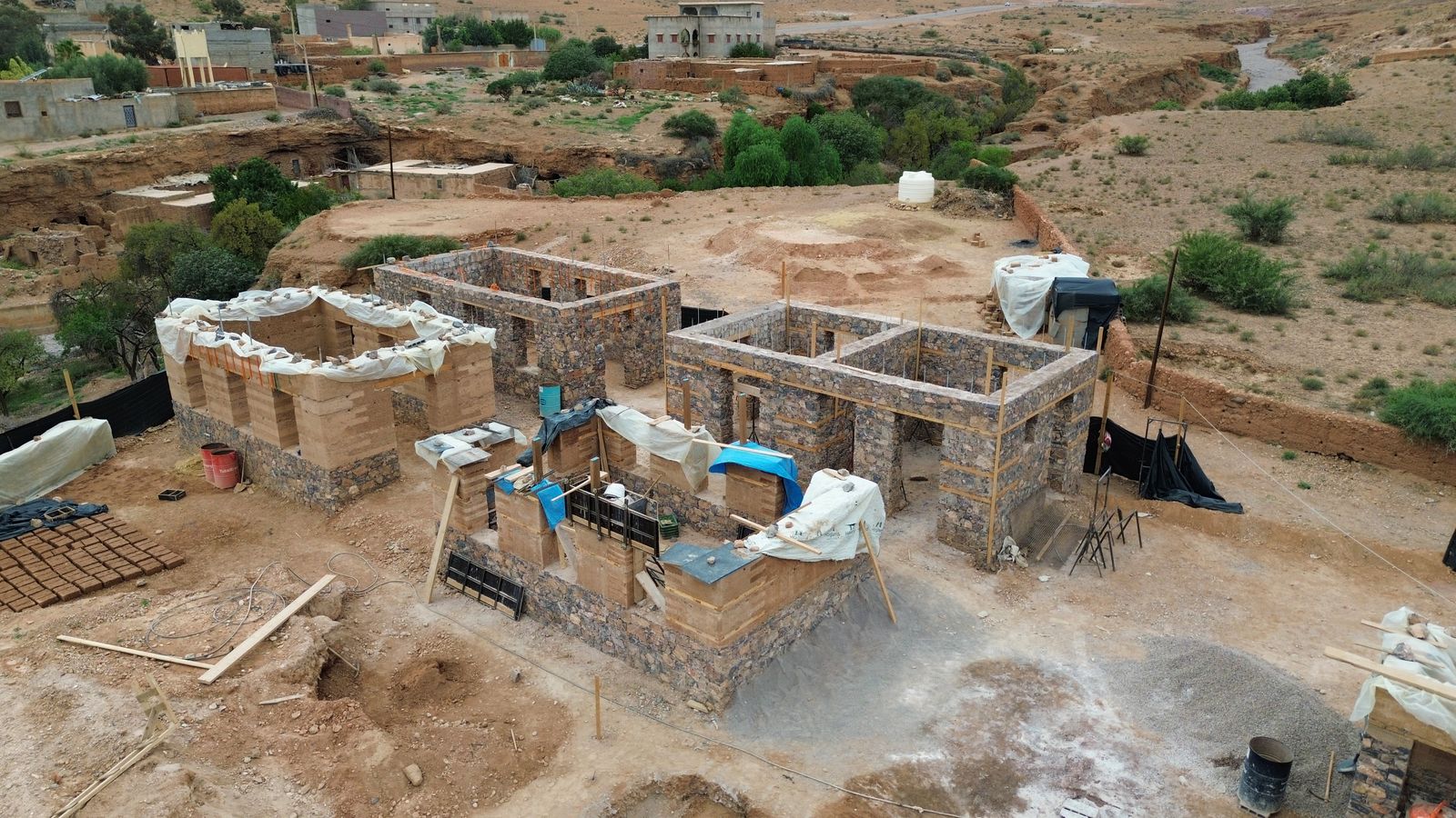 Vue aérienne du chantier de Taliouine : bâtiments en pierre et en pisé, douar et ravin en arrière-plan